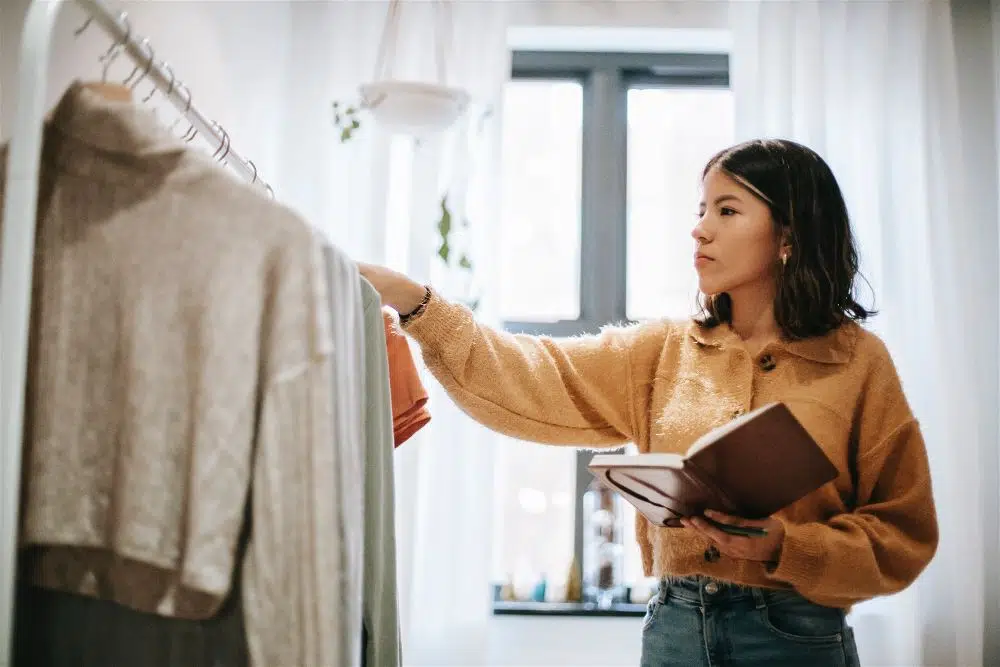 mulher fazendo controle de estoque de roupas da loja, segurando um caderno na mão