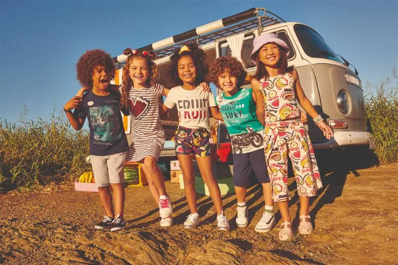 5 crianças sorrindo abraçadas no meio da natureza