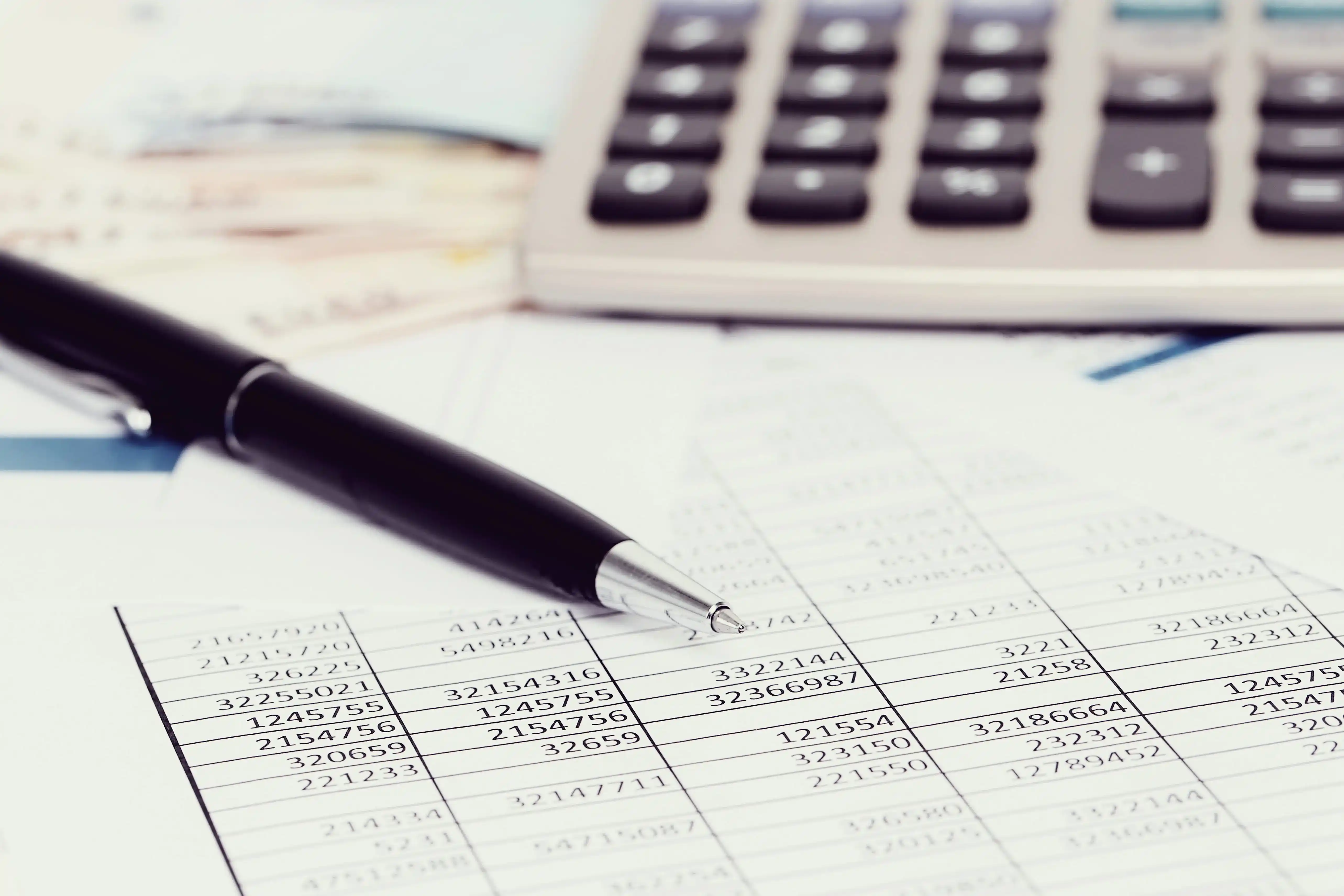 papel com alguns dados numéricos, com uma caneta e calculadora por cima