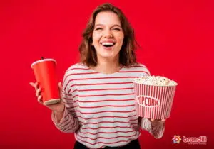 mulher sorrindo para a câmera segurando um refrigerante e um balde de pipoca