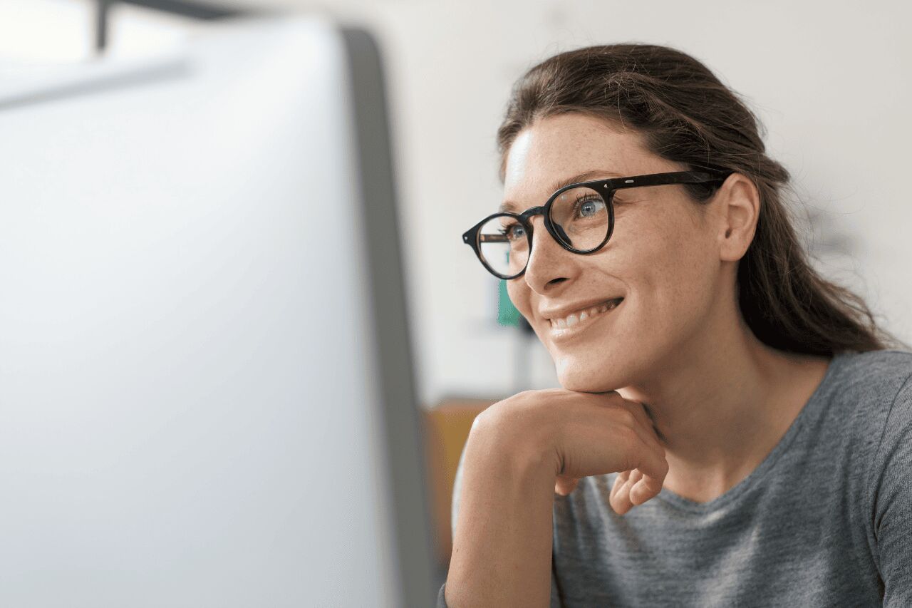 Mulher sorridente usando óculos e olhando para o computador.