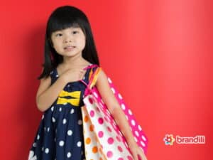 Menina asiática sorri enquanto segura sacolas de roupa