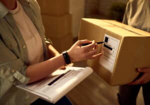 mulher segurando caixa de papelão e outra mulher verificam dados sobre os pacotes de entrega