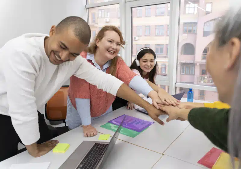 equipe de trabalho dando risada juntando as mãos no centro da mesa 