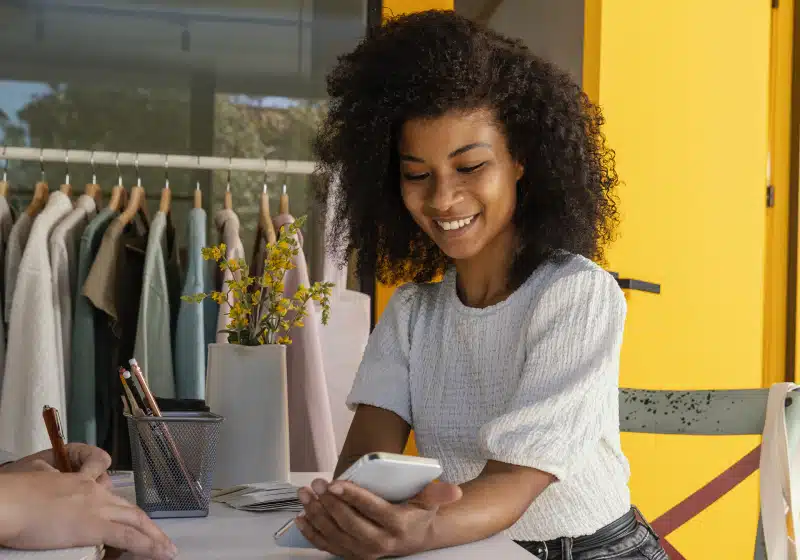 mulher negra empreendedora sorridente mexendo no celular 