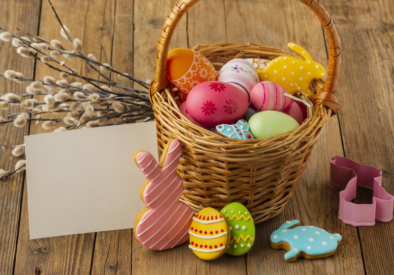 ovos de pascoa coloridos em uma cesta com coelhinho de chocolate com envelope de papel ao lado
