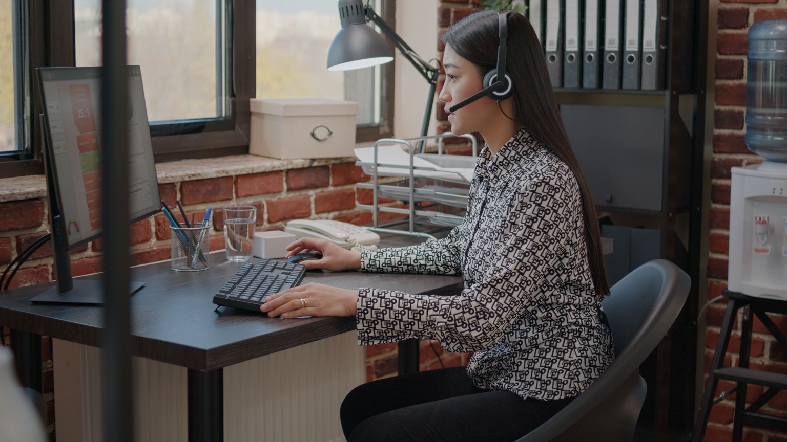 Mulher trabalhando em frente ao computador com fone de ouvido na orelha