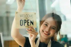 empresária segura placa escrito "open" (aberto, em inglês), comum em vários tipos de comércio