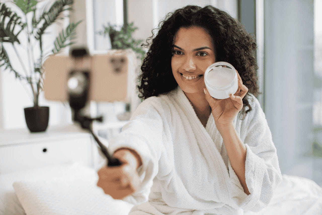 mulher de roupão mostrando cosmético para câmera