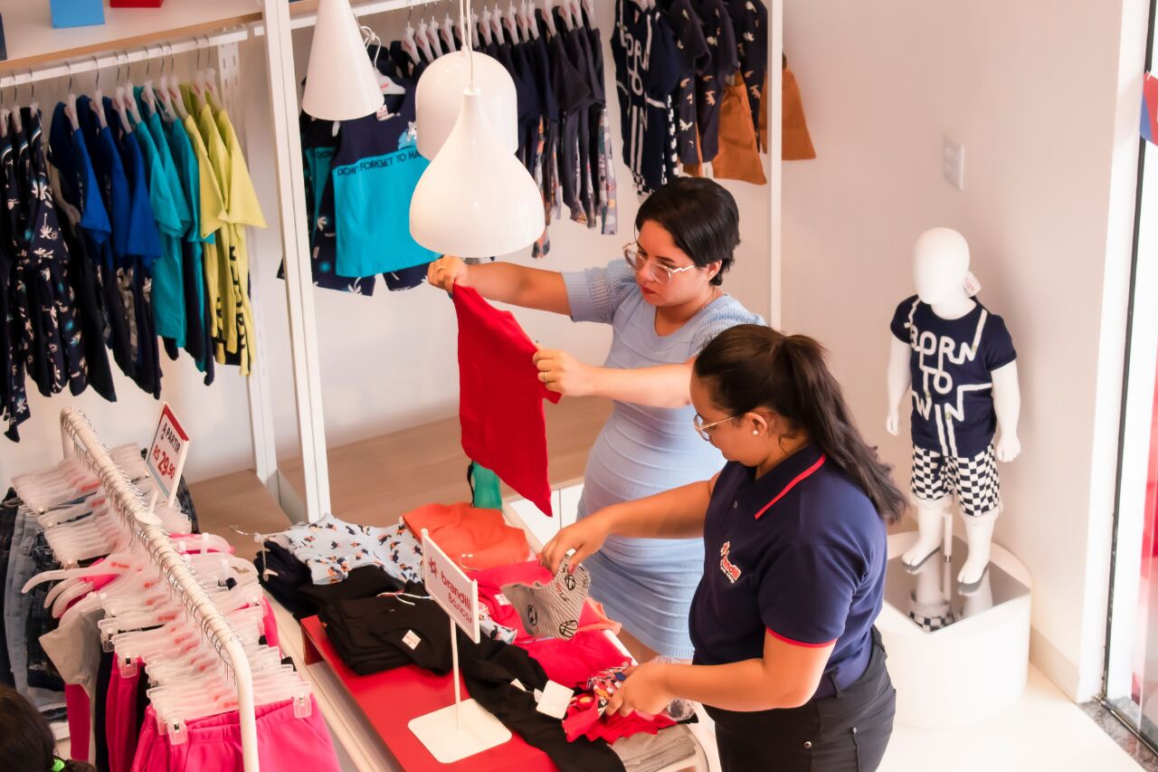 Duas mulheres organizando roupas em loja de roupas infantis
